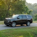 A black 2021 Chevy Tahoe High Country is driving on a road next to a pond and trees.