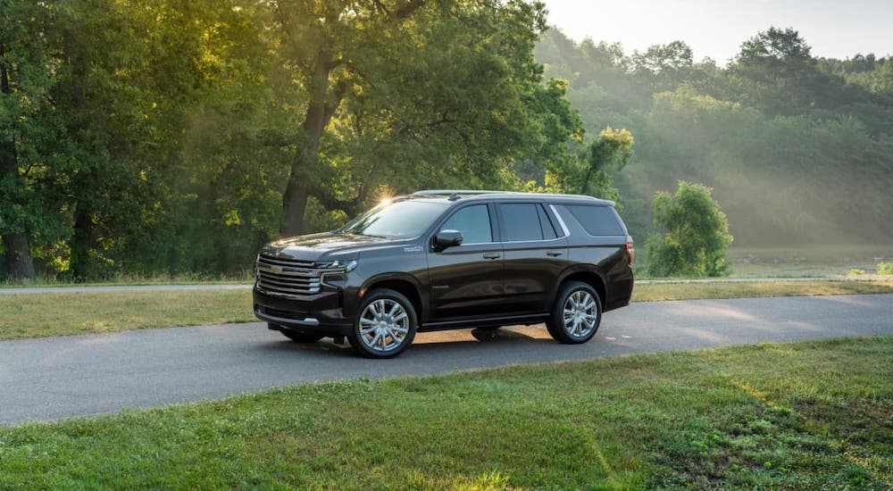 A black 2021 Chevy Tahoe High Country is driving on a road next to a pond and trees.