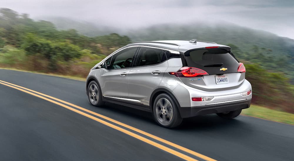 A silver 2021 Chevy Bolt EV, a popular 2021 electric vehicle, is driving past misty mountains.