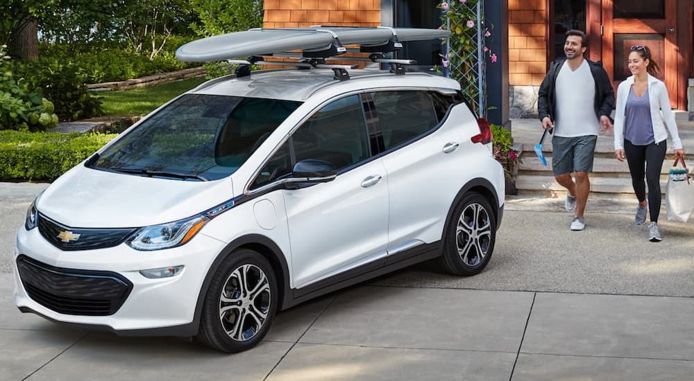 A couple is walking toward a white 2021 Chevy Bolt EV in a driveway.