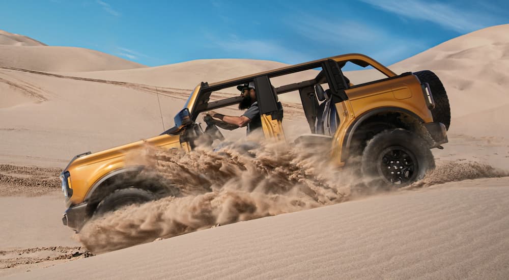 A yellow 2021 Ford Bronco 4-door with not roof or doors is off-roading on a sand dune.