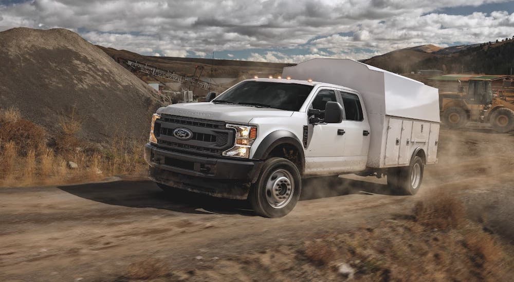 A white 2021 Ford Chassis Cab F-450 with toolbox is driving in front of a dirt pile.