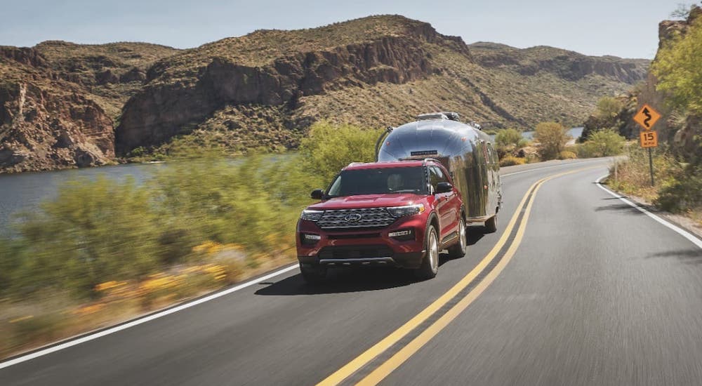 A red 2021 Ford Explorer is towing an Airstream camper on a highway.