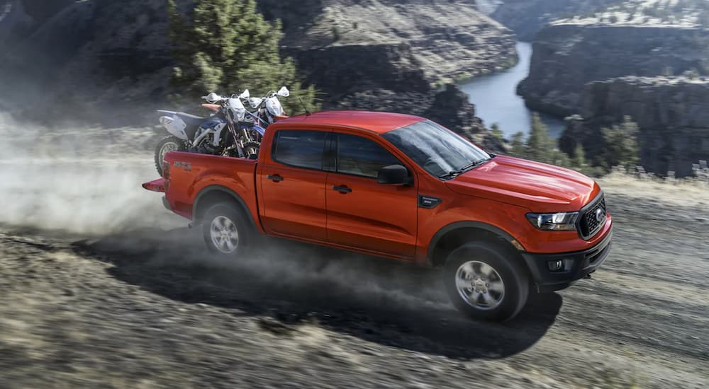 A red 2021 Ford Ranger is driving on a dirt road with dirt bikes in the bed.