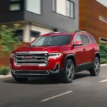 A red 2021 GMC Acadia is shown driving past modern buildings.
