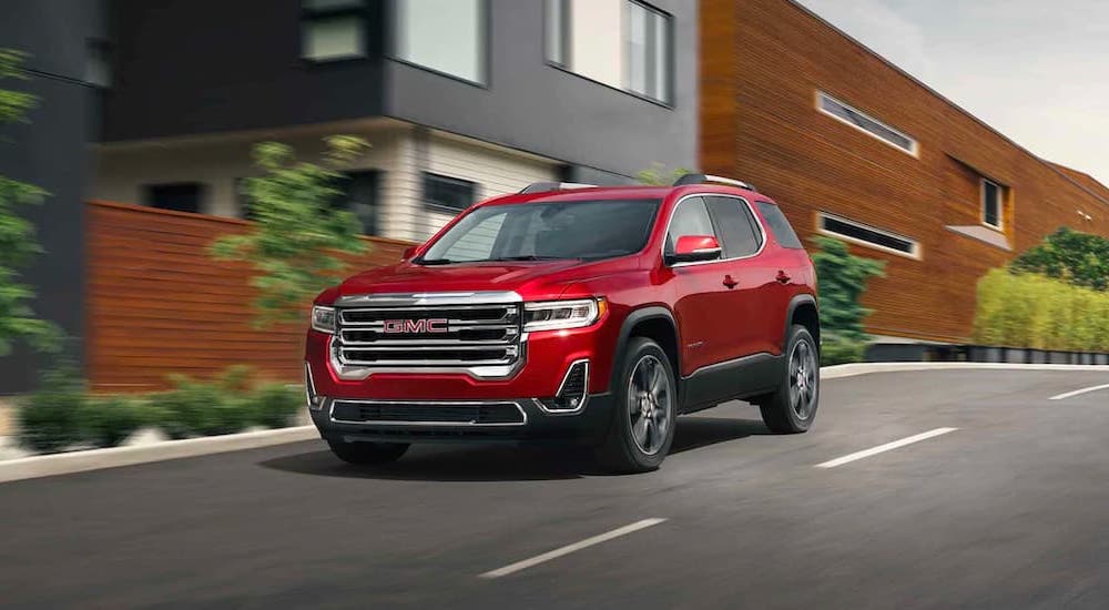 A red 2021 GMC Acadia is shown driving past modern buildings.