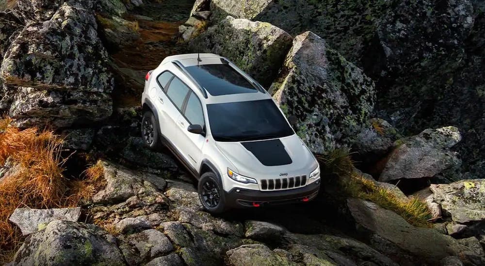 A white 2021 Jeep Cherokee Trailhawk is driving on rocks from a high angle.