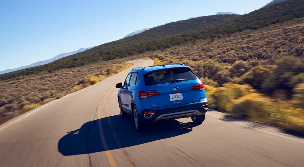 A blue 2022 Volkswagen Taos is shown from the rear driving on an empty desert road.