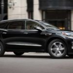 A black 2021 Buick Enclave is driving past a white building after leaving a Buick dealer.