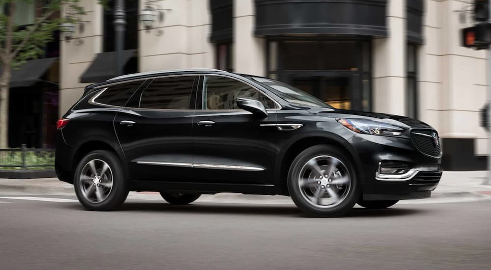 A black 2021 Buick Enclave is driving past a white building after leaving a Buick dealer.