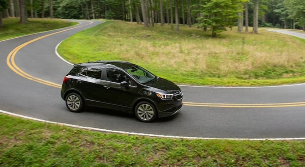 A black 2021 Buick Encore is driving around a horseshoe corner on a rural road.