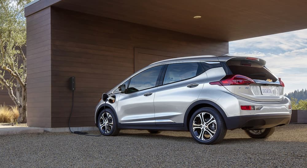 A silver 2021 Chevy Bolt EV is charging at a modern house.