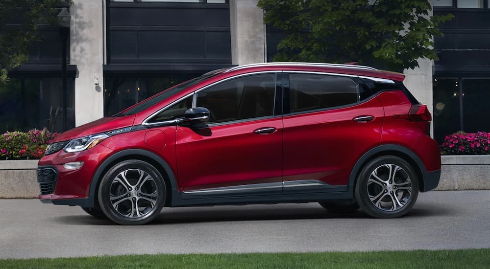 A popular Chevy EV, a red 2021 Bolt EV, is shown from the side in front of a building.