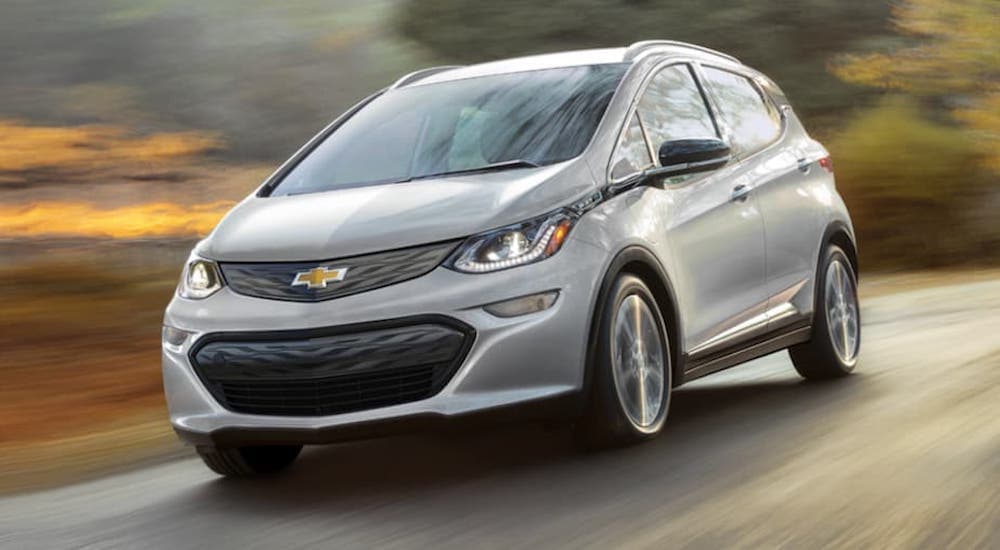A silver 2021 Chevy Bolt EV is driving on a blurry rural road.