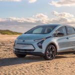 A new model of a classic Chevy EV, a pale blue 2022 Chevy Bolt EV, is parked on a beach.