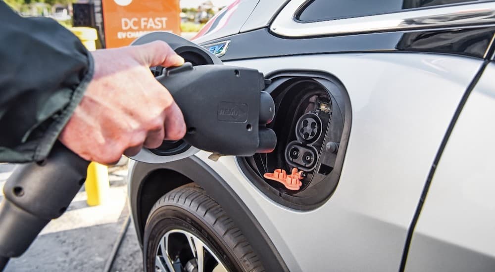 A closeup shows a charger being plugged into a silver 2018 Chevy Bolt EV.