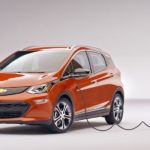 An orange 2020 Chevy Bolt EV is charging with a white background.