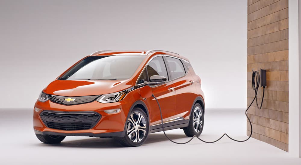 An orange 2020 Chevy Bolt EV is charging with a white background.