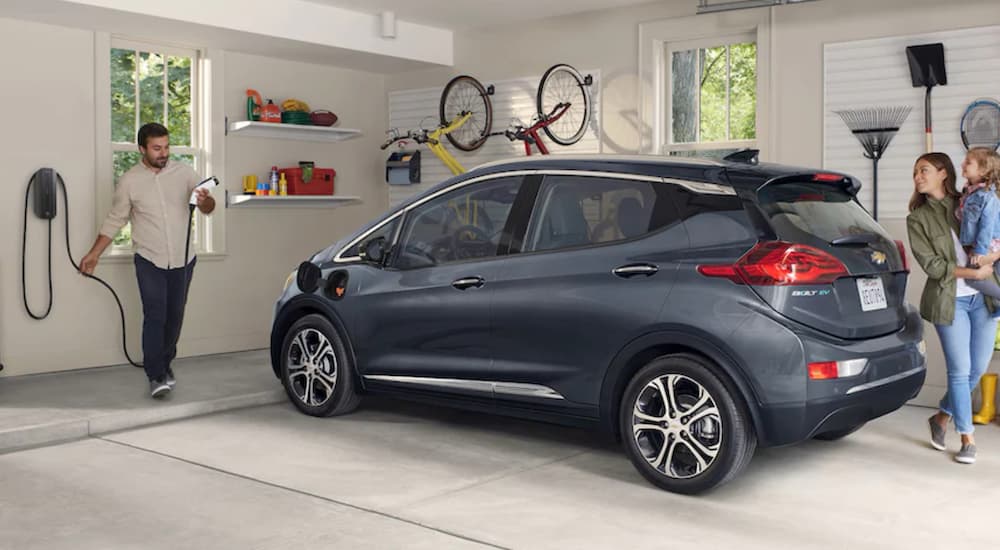 A family is in a garage with a grey 2020 Chevy Bolt EV after leaving a Chevy EV dealer.