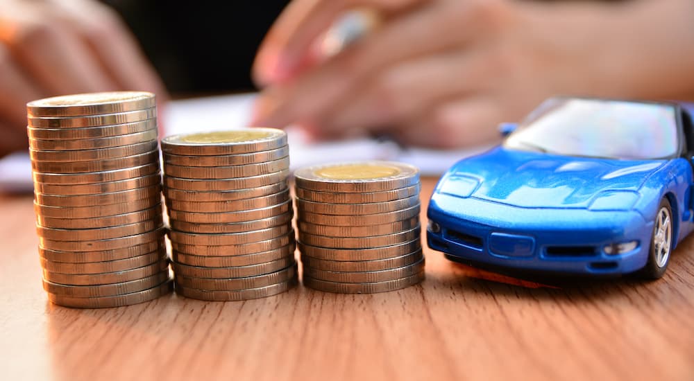 A blue die-cast car is on a wooden table next to three stacks of coins.