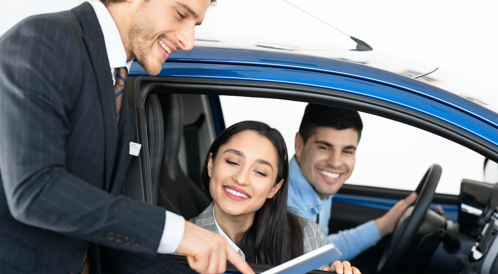 A couple is looking over paperwork with a salesman with sitting in a blue used car.