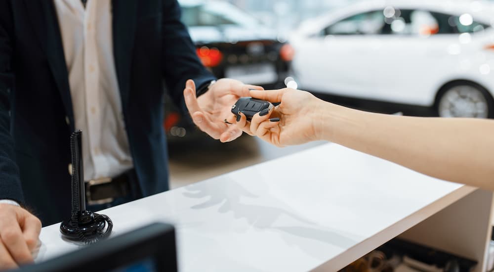 A close up shows a pair of hands exchanging a set of car keys at a car dealership.