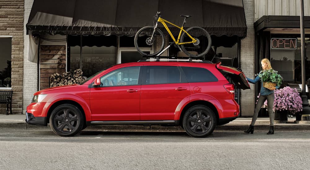 A woman is loading the trunk of a 2020 Dodge Journey with a yellow bike on the roof on a city street.