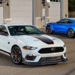 A white and a blue 2021 Ford Mustang Mach 1 are parked in front of a garage.