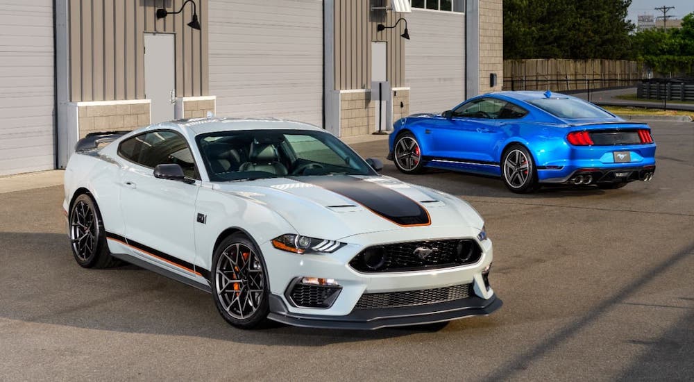 A white and a blue 2021 Ford Mustang Mach 1 are parked in front of a garage.