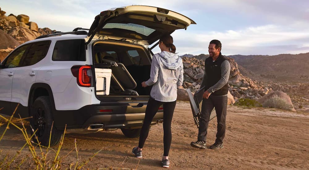 A white 2021 GMC Acadia AT4 is shown with a couple loading chairs into the trunk.