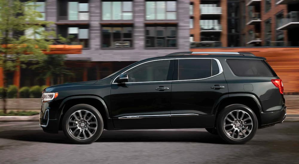 A black 2021 GMC Acadia Denali is shown from the side driving through the city after leaving a GMC dealer near you.