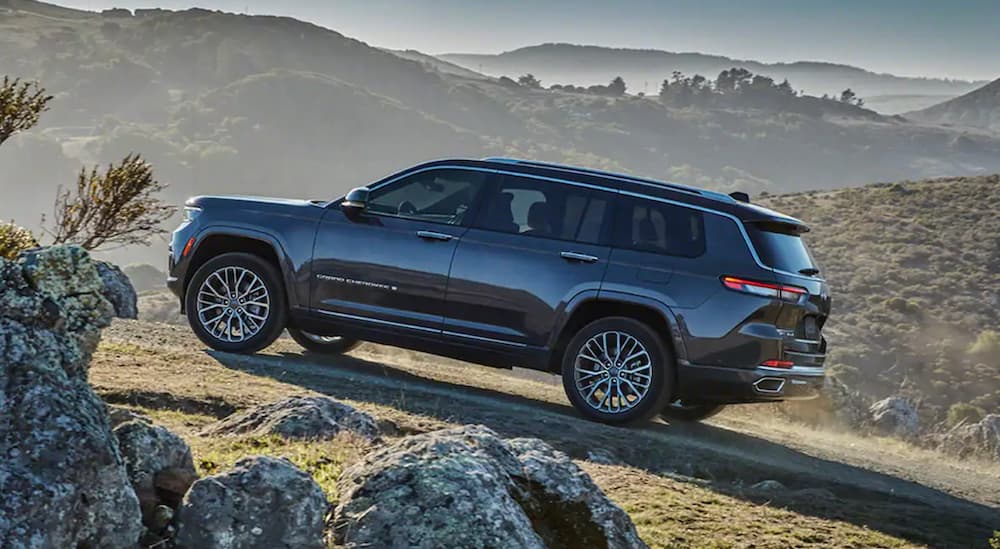 A black 2021 Jeep Grand Cherokee L is driving on a dirt path past mountains.