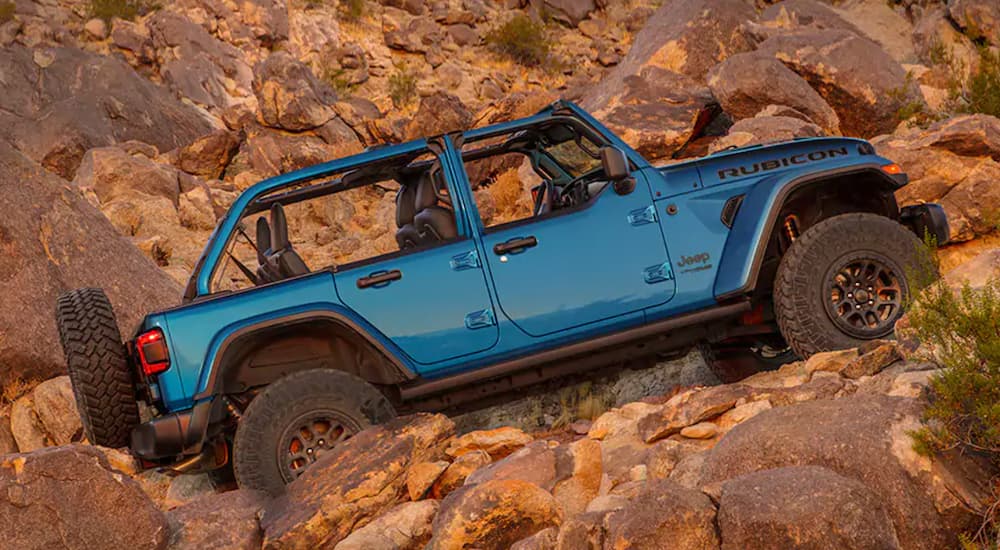 A blue Jeep Wrangler Rubicon 392 is shown from the side off-roading on desert rocks after leaving a Jeep dealer.