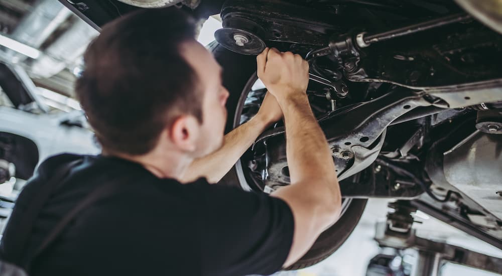 A man is shown from a low angle with a ratchet wrench, working on a vehicle sitting on a lift.