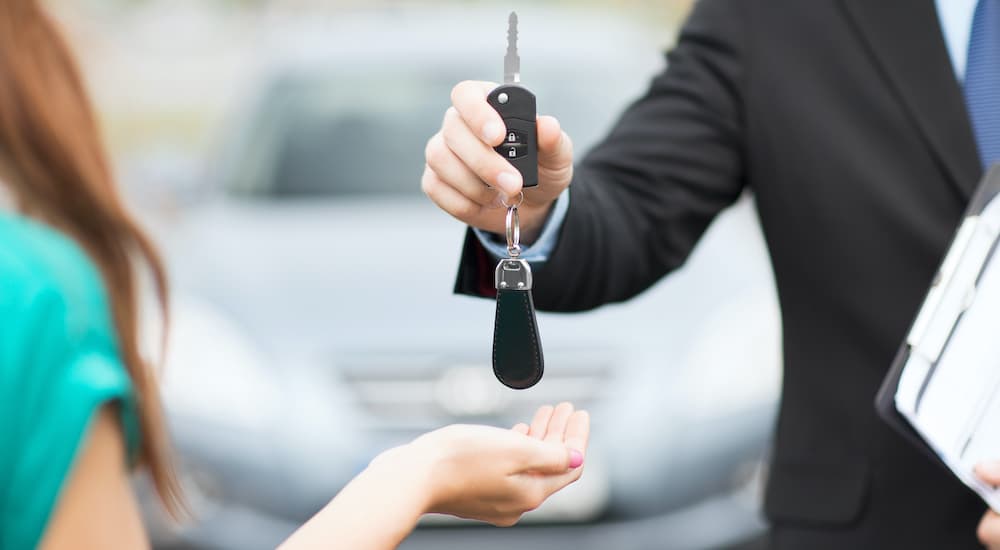 A salesman is handing a woman a set of car keys.