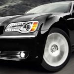 A popular used car, a black 2012 Chrysler 300, is shown driving on a highway in a closeup.