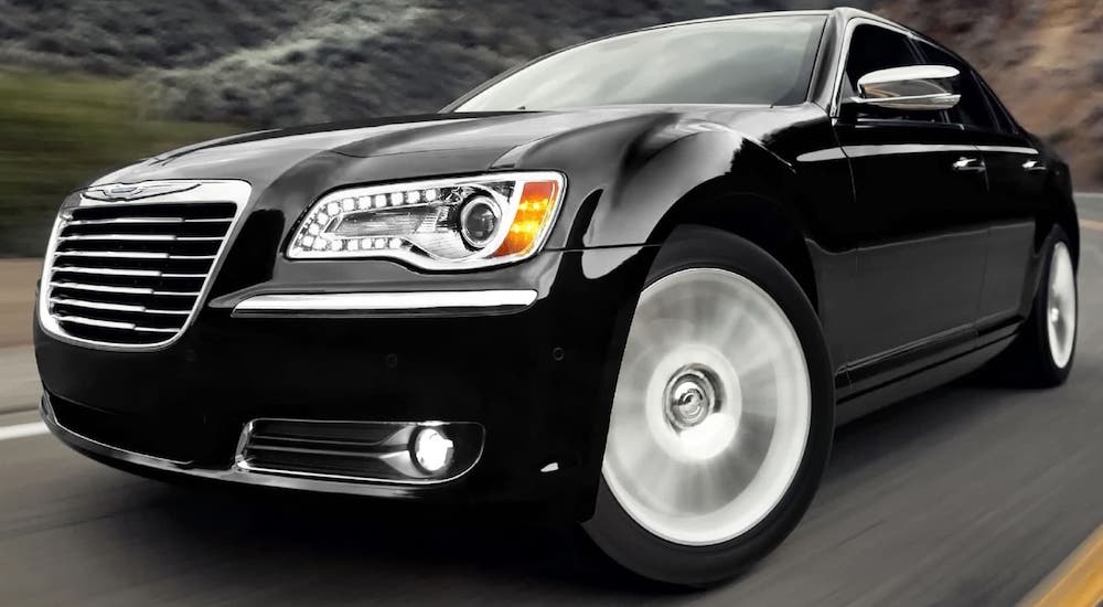 A popular used car, a black 2012 Chrysler 300, is shown driving on a highway in a closeup.