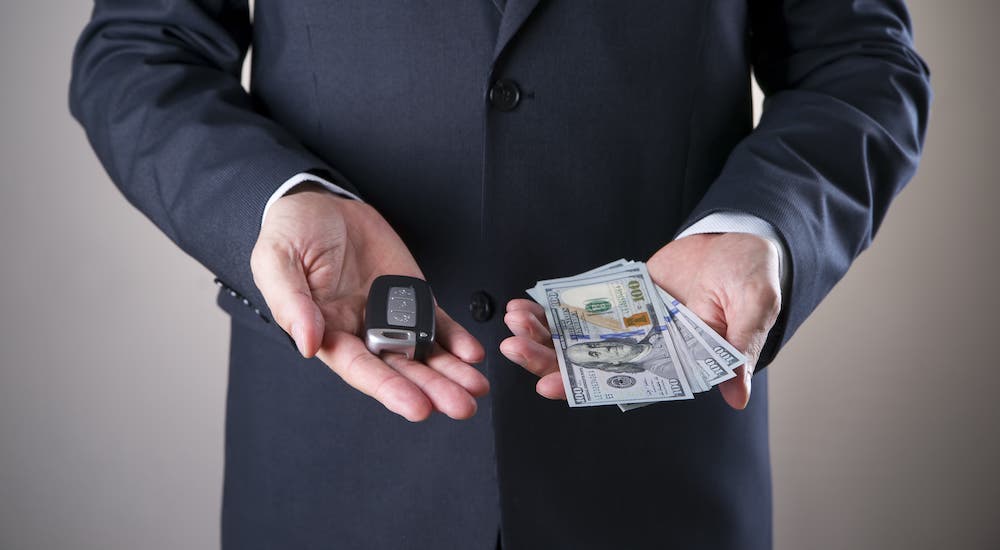 A man in a suit is holding a car key and several hundred dollar bills.