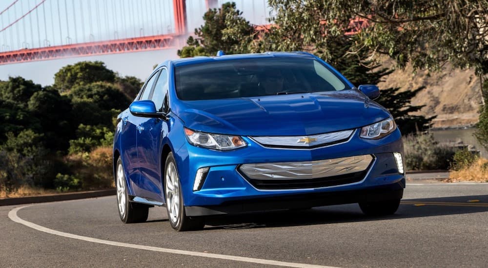 A blue 2018 Chevy Volt is driving around a corner in front of the Golden Gate Bridge.