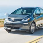 A popular used Chevy EV, a grey 2019 Chevy Bolt EV is driving past the ocean.