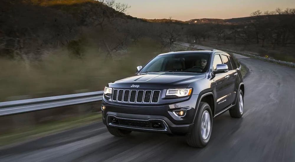 A gray 2011 Jeep Grand Cherokee is driving on track at dusk.