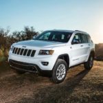 A white 2011 Jeep Grand Cherokee from a used Jeep Grand Cherokee dealer is driving on a dirt trail.