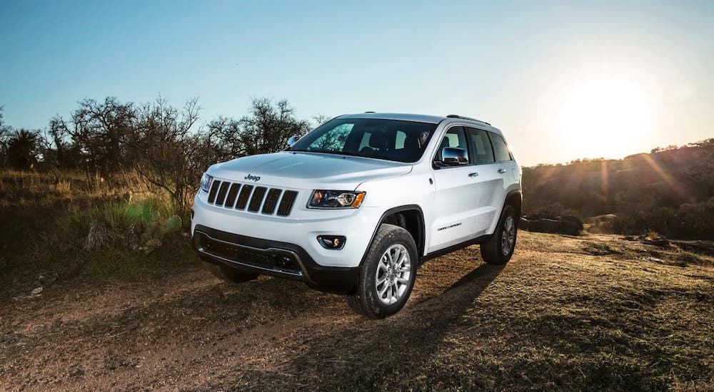 A white 2011 Jeep Grand Cherokee from a used Jeep Grand Cherokee dealer is driving on a dirt trail.