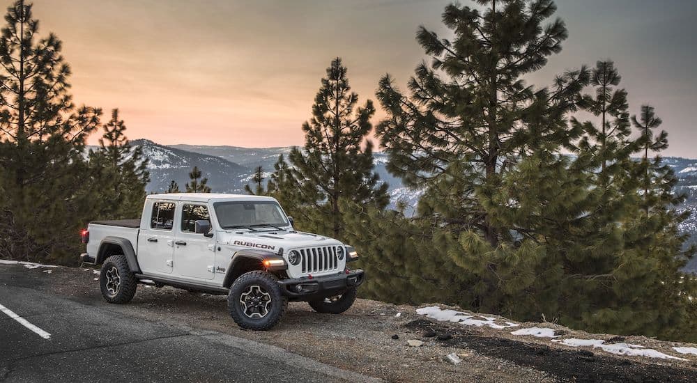 A white 2020 Jeep Gladiator is parked in front of trees and snow-covered mountains.