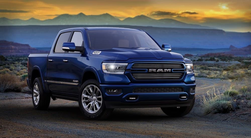 A blue 2020 Ram 1500 is parked in front of a desert and a colorful blue and yellow sky.