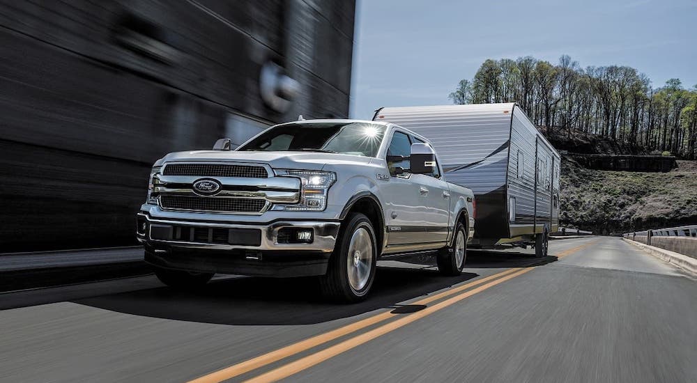 A white 2017 Ford F-150 is towing a camper on a city street.