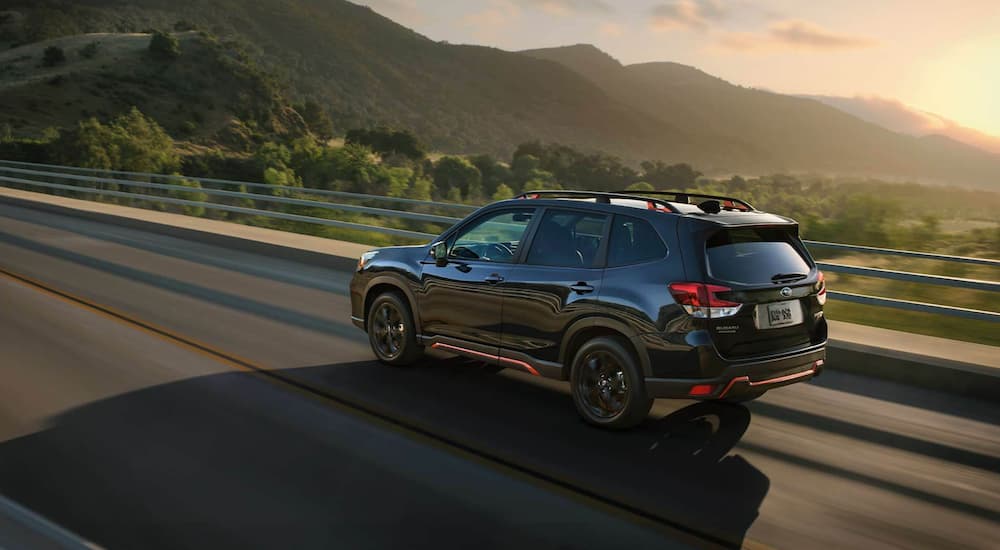 A black 2021 Subaru Forester is shown from the side driving on an open road as the sun sets.