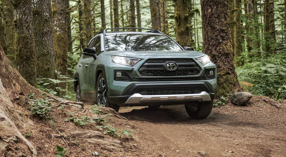 A light green 2021 Toyota RAV4 is off-roading on a path in the woods.
