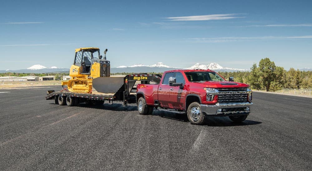 A red 2021 Chevy Silverado 3500HD is parked on an empty lot with a trailer and construction equipment.