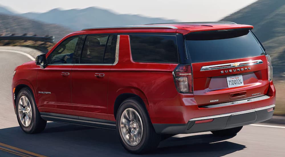 A red 2021 Chevy Suburban is driving on a road with mountains in the background.